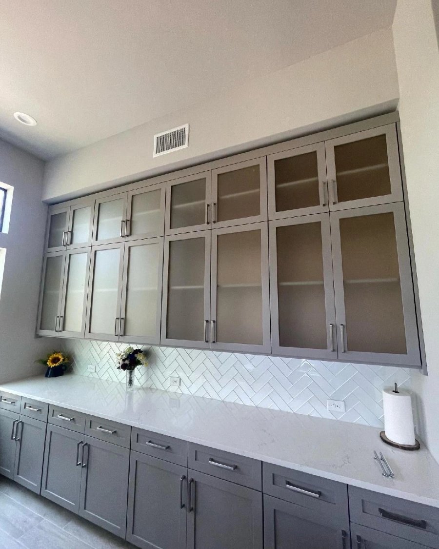 Modern gray kitchen cabinets with glass doors and white herringbone tile backsplash.