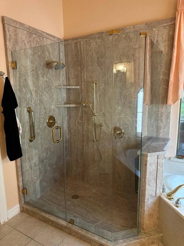 Elegant glass-enclosed marble shower with gold fixtures.