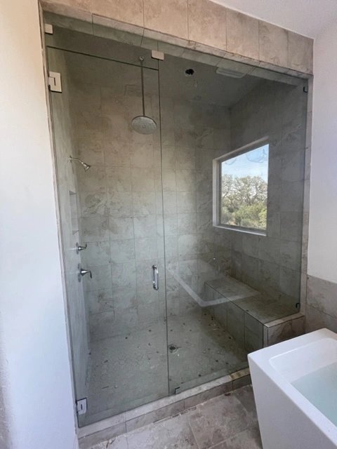 Modern tiled bathroom shower with glass enclosure and bench seat.