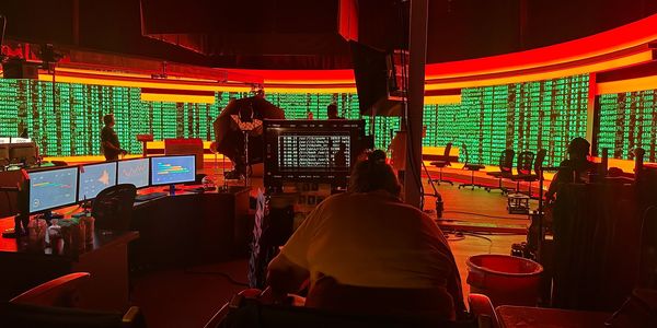 Person working in a dark room with multiple monitors and a data display wall.