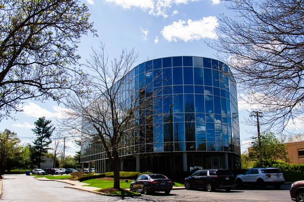Modern glass office building with parked cars and trees around.