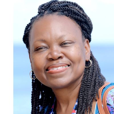 Smiling woman with braided hair and hoop earrings against a light blue background.