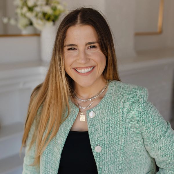 Smiling woman in a green blazer and black top posing indoors.