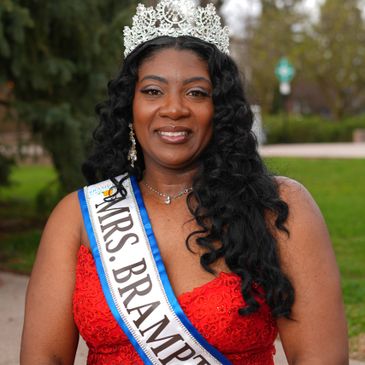 A woman wearing a crown and Mrs. Brampton sash smiles outdoors.