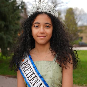 Young girl wearing a crown and preteen sash outdoors.