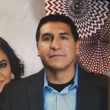 Man in a blue shirt and dark blazer posing indoors.