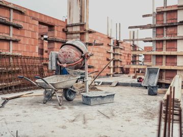 Construction site with cement mixer and wheelbarrow on concrete floor.