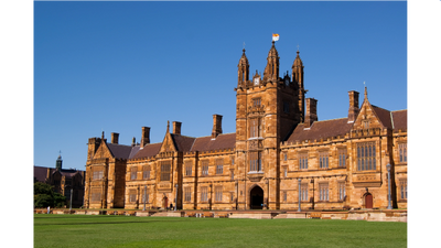 Historic sandstone university building with a central tower under clear blue sky.