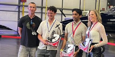 Four people posing with racing trophies and medals in a garage.