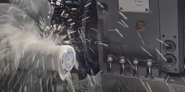 CNC machine cutting a cylindrical object with coolant spraying.