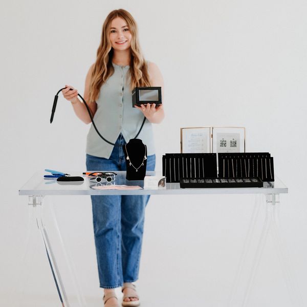 Woman showcasing jewelry and tools at a transparent table.