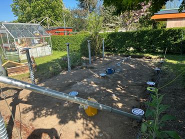 Garden area with metal posts and a greenhouse in the background.