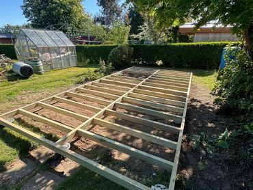 Wooden frame foundation laid out on garden soil under clear sky.