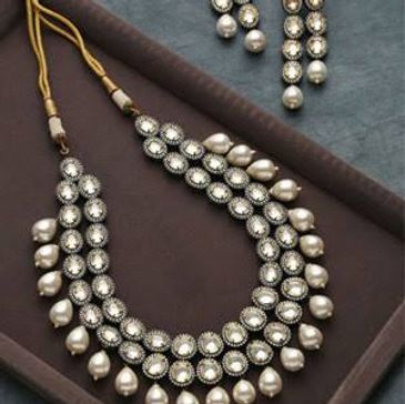 Elegant pearl and stone necklace with matching earrings on a dark tray.