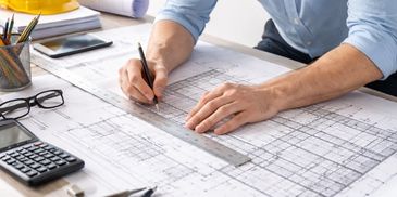 Person working on architectural blueprints with a ruler and pencil.