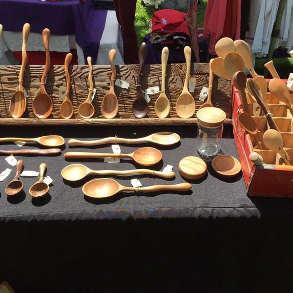 Handcrafted wooden spoons and kitchen utensils displayed on a black cloth at a market stall.