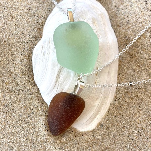 Two sea glass pendants, green and brown, on silver chains.