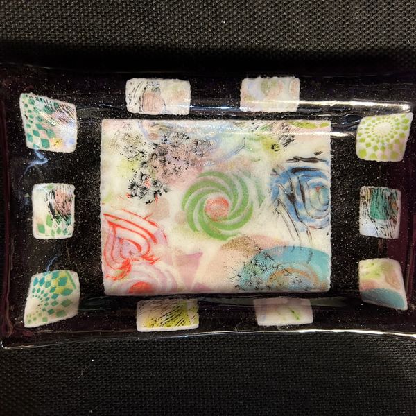 Rectangular glass dish with colorful abstract patterns on a black background.