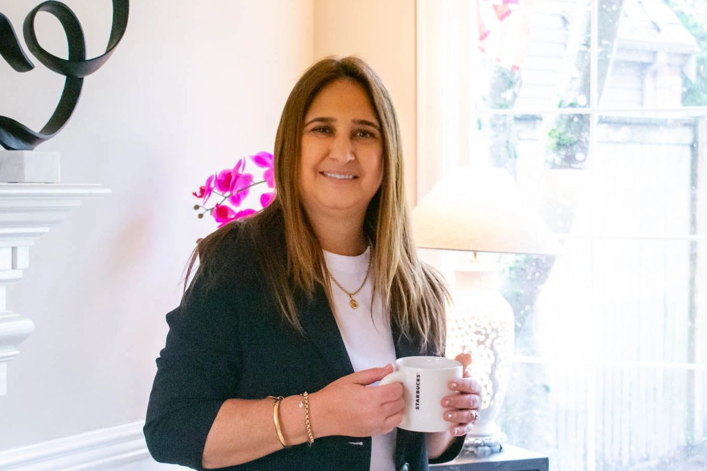 A woman smiling and holding a Starbucks mug indoors.