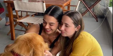 Two women happily interacting with a golden retriever indoors.