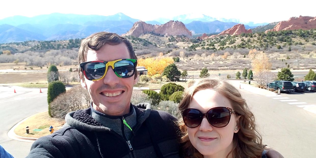 Couple smiling with sunglasses outdoors and mountains in the background.