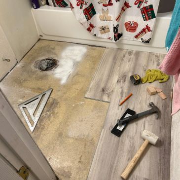 Bathroom floor being renovated with wood-like vinyl planks and tools scattered.