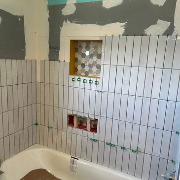 Partially tiled bathroom wall with bathtub and hexagonal tile niche.