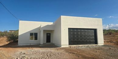 Modern white house with black garage door in a dry, rocky terrain.