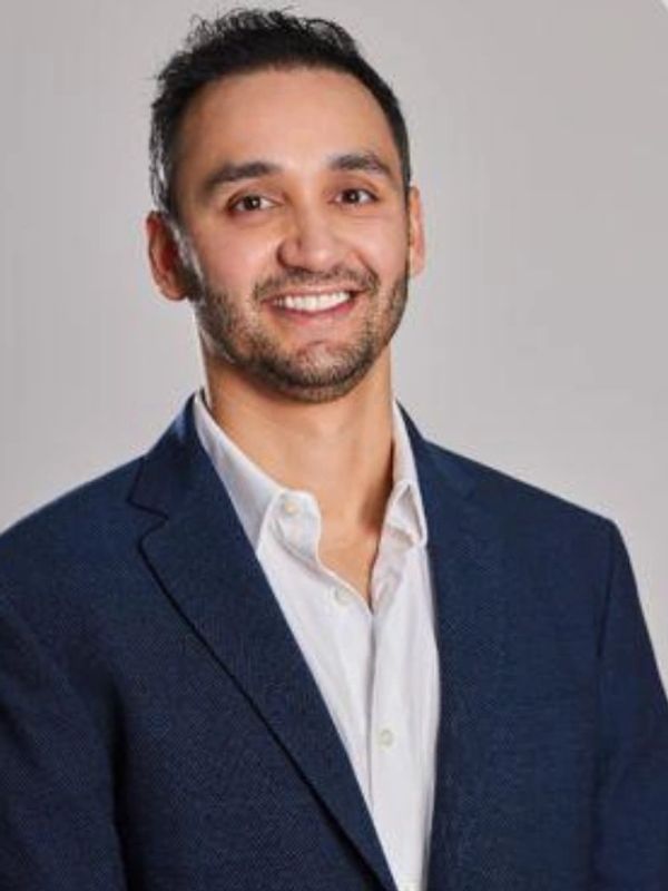 Smiling man in a navy blue blazer and white shirt.