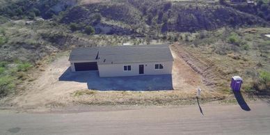 A small house with a garage and portable toilet in a barren area.