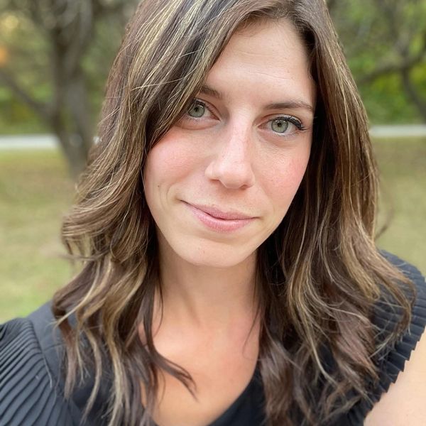 Close-up portrait of a woman with wavy brown hair and green eyes outdoors.