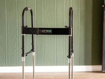 A black and silver folding walker against a green wall.