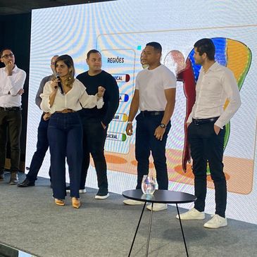 Group of five people presenting on stage with a colorful screen behind them.