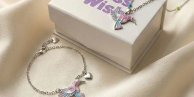 Silver hummingbird-themed necklace and bracelet on a silk fabric.