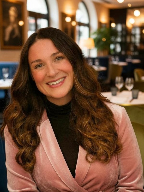 Smiling woman in a pink blazer seated in a cozy restaurant.