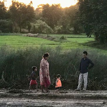 A family of four walking near a grassy field at sunset.