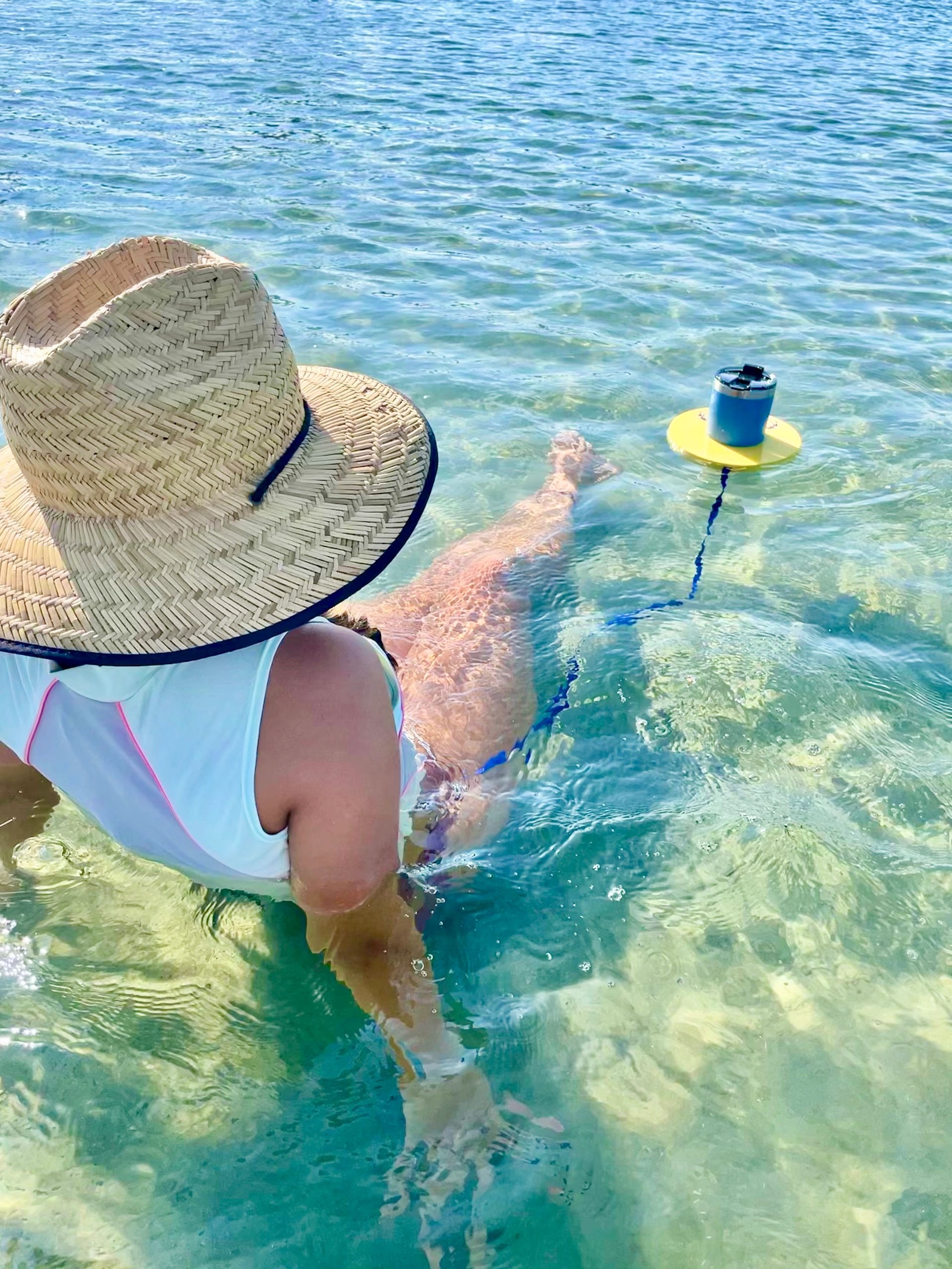 A woman lounging in a tidal pool with her Tumbler Tube, the perfect drink float, beside her.