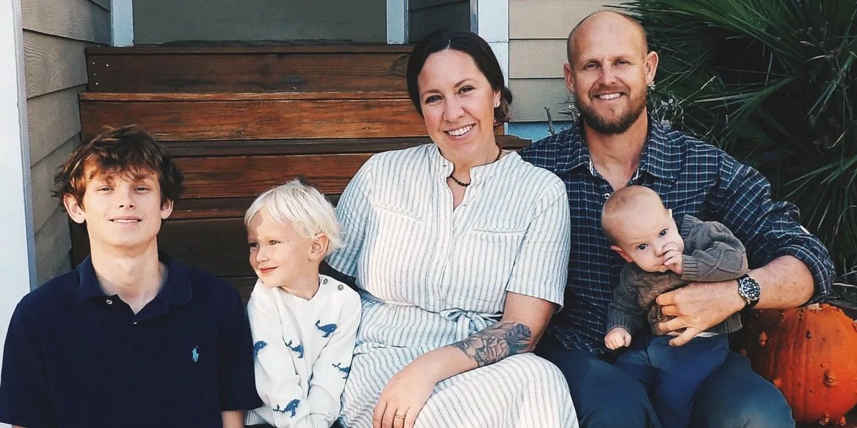 A family of 5, husband, wife, teenage son, & 2 young boys, sitting on a porch together smiling.