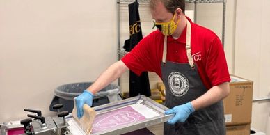 shows image of someone screen printing community event tee shirts.
