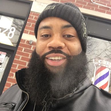 Man with a beard and beanie smiling outside a barbershop.