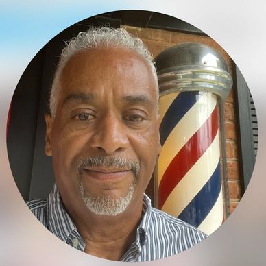 Smiling man with gray hair in front of a classic barber pole.