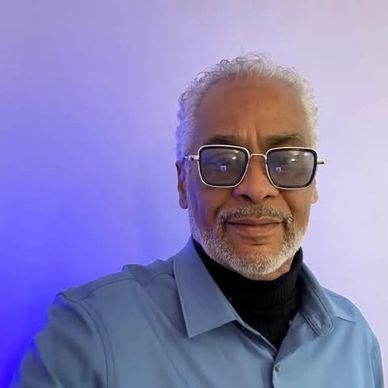 Smiling elderly man with glasses against a blue-purple gradient background.