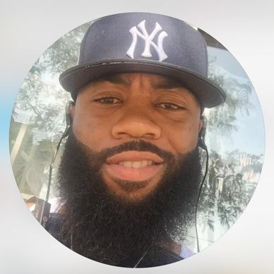 Man with a beard wearing a New York Yankees cap and earphones.