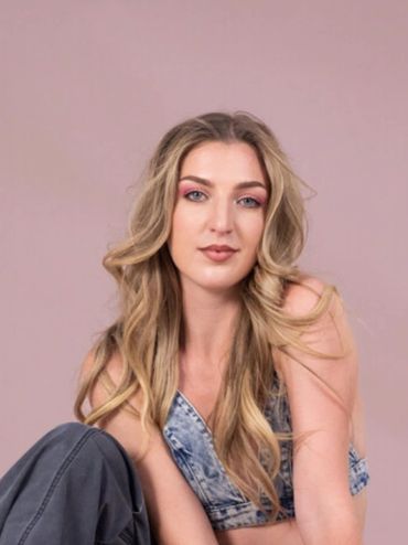 Young woman with long blonde hair posing against a pink background.