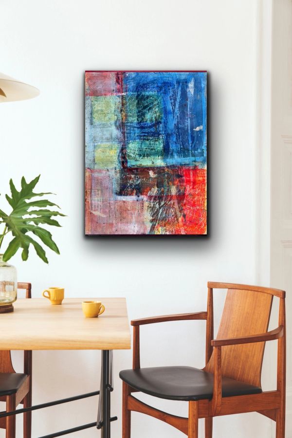 Colorful abstract painting on a white wall above a wooden table and chair.