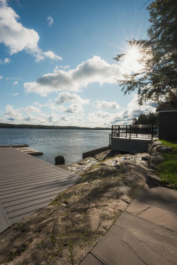 Sun shining over a rocky riverbank with dock and railing.