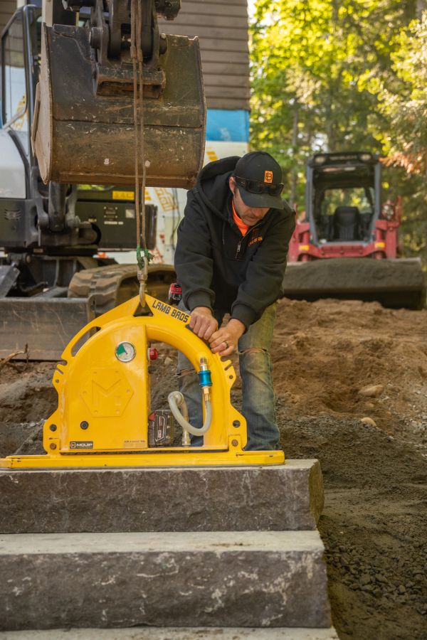 A construction worker operating a yellow lifting device on stone blocks.