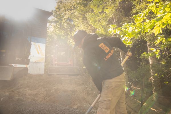 Worker shoveling dirt outdoors in bright sunlight.