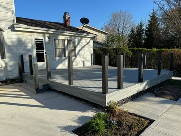 Newly built gray wooden deck attached to a white house in a sunny backyard.