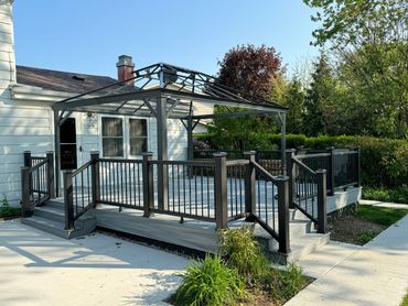 A modern backyard deck with black railings and a metal pergola frame.